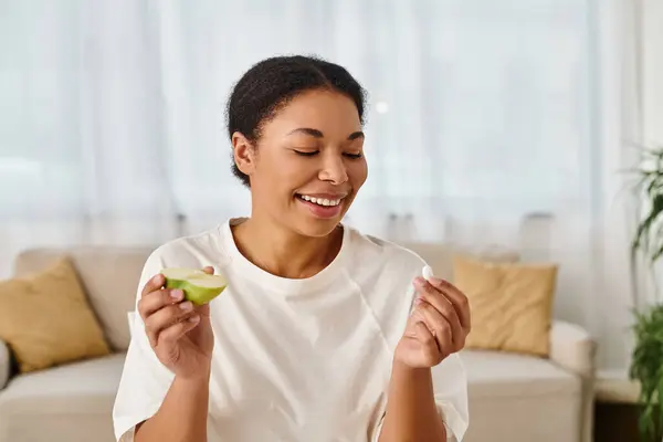 Happy african american nutritionist compares supplements with fresh apple for a healthy diet — Stock Photo