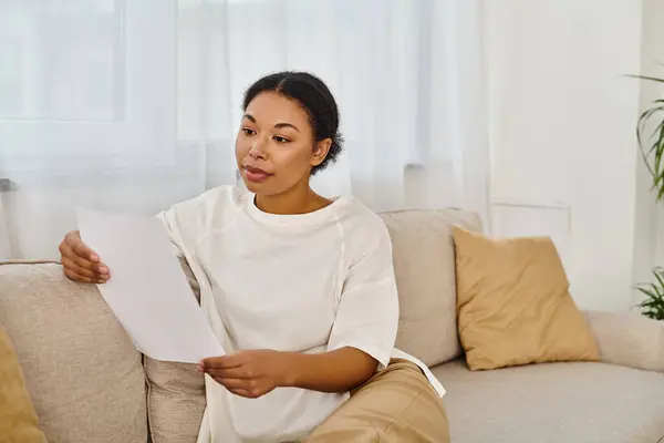 Кудрявая африканская американка в повседневной одежде читает рецепт на диету и расслабляется на диване — стоковое фото