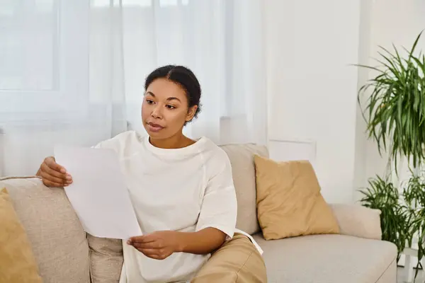 Brunette afro-américaine en tenue décontractée lecture prescription alimentaire et détente sur canapé — Photo de stock