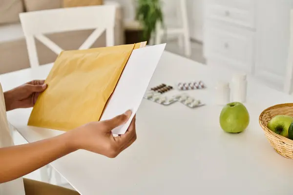 Cropped view of black woman reviewing dietary plan while opening envelope near supplements — Stock Photo