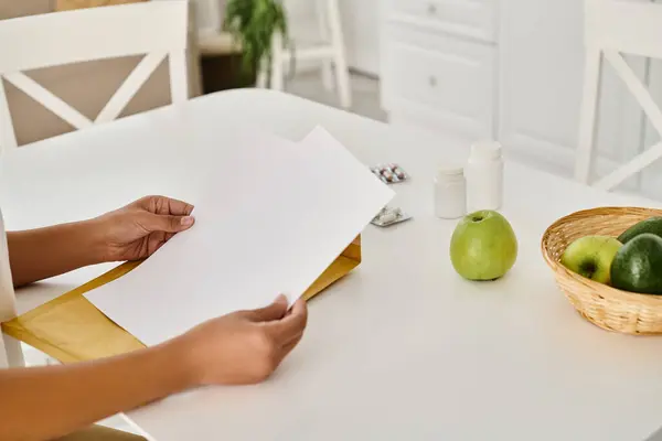 Cropped african american woman reviewing dietary plan near supplements and fruits on kitchen table — Stock Photo