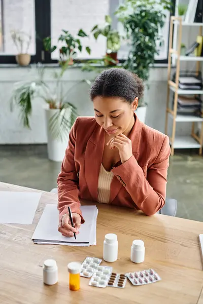 Smiling african american nutritionist evaluating medication while writing notes in her office — Stock Photo