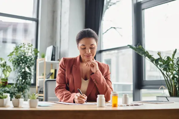 Pleased african american nutritionist evaluating medication while writing notes in her office — Stock Photo