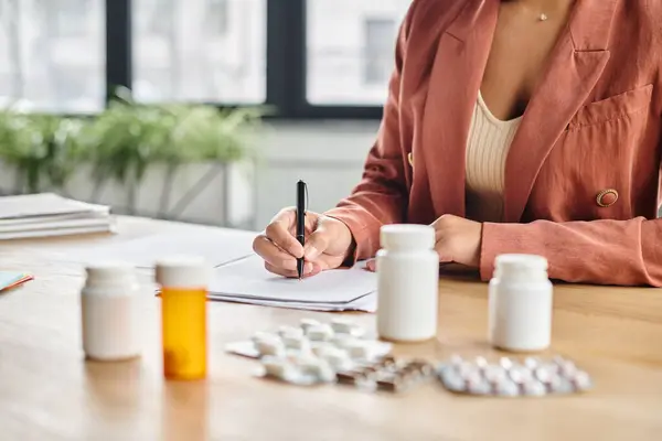 Nutricionista afro-americana cultivada avaliando medicação enquanto escrevia notas em seu escritório — Fotografia de Stock