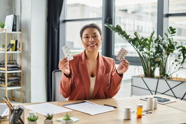 Joyful african american nutritionist showing different medication while sitting in her office — Stock Photo