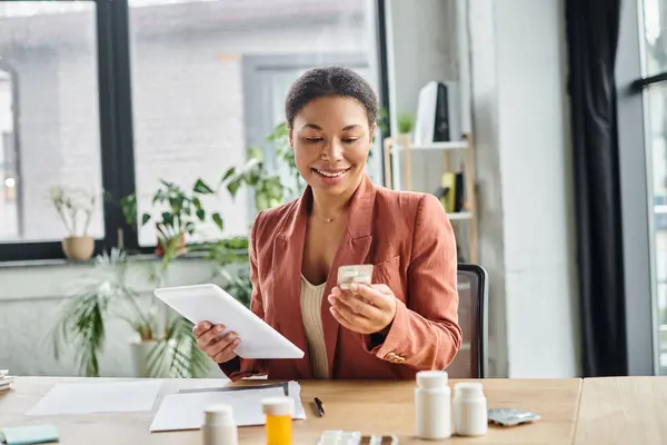 Joyful african american dietitian using tablet while organizing supplements in a green office — Stock Photo