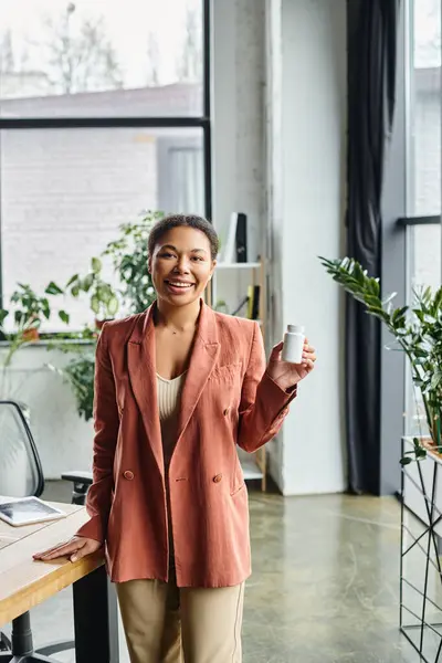 Happy african american dietitian holding bottle with supplements and smiling in a bright office — Stock Photo