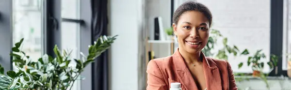 Dietista afroamericano feliz sosteniendo la botella con suplementos y sonriendo en la oficina, pancarta - foto de stock