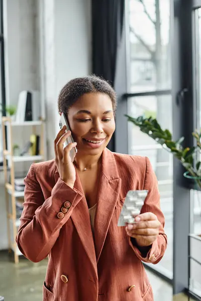 Consultoría nutricionista afroamericana feliz a través de teléfono inteligente mientras analiza suplementos en la oficina - foto de stock