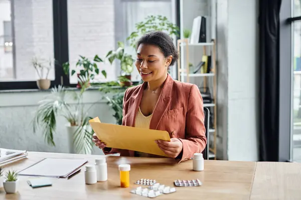 Positive african american dietitian reviewing envelope near supplements on her working desk — Stock Photo