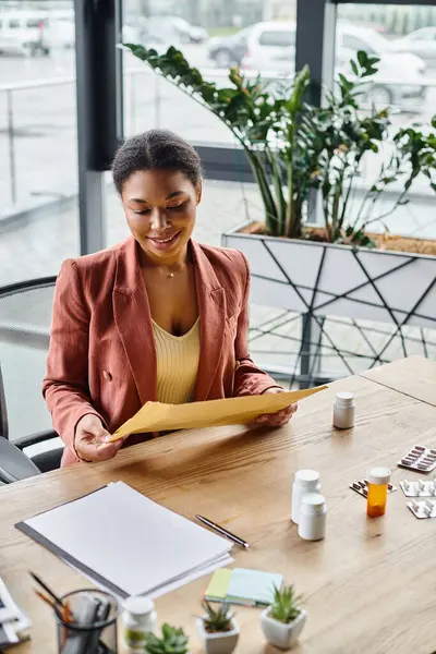 Happy african american dietitian reviewing envelope near supplements on her working desk — Stock Photo