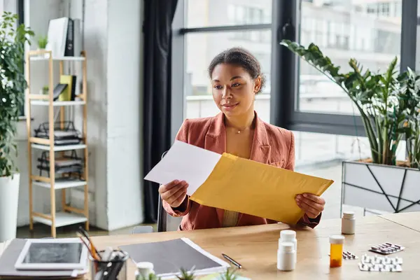 Focused african american dietitian reviewing envelope near supplements on her working desk — Stock Photo