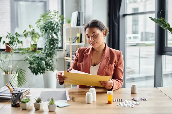 Focused african american nutritionist reviewing envelope near supplements on her working desk — Stock Photo
