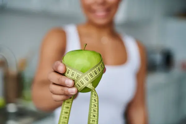 Cropped happy african american woman with measuring tape and apple promoting a healthy diet — Stock Photo