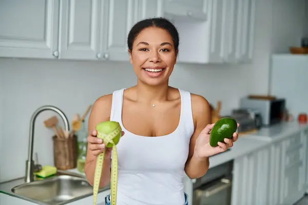 Fröhliche afrikanisch-amerikanische Frau mit Maßband und Früchten, die für eine gesunde Ernährung in der Küche wirbt — Stockfoto