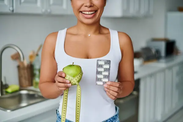 Beschnitten glückliche afrikanisch-amerikanische Frau mit Maßband mit Apfel und Packung mit Nahrungsergänzungsmitteln — Stockfoto