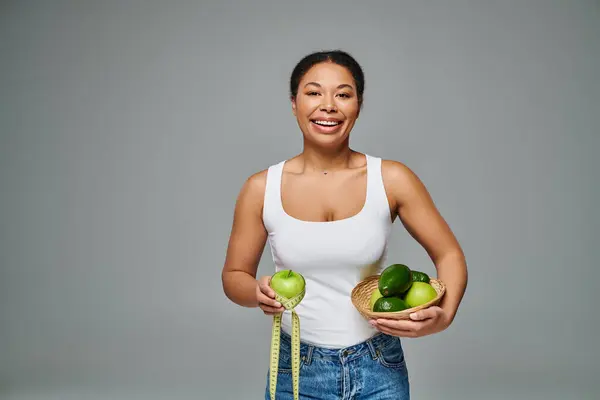 Heureuse diététiste afro-américaine avec pomme et suppléments mettant en valeur la santé sur fond gris — Photo de stock