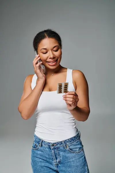 Felice consulente nutrizionista afro-americano tramite smartphone e con integratori in grigio — Foto stock