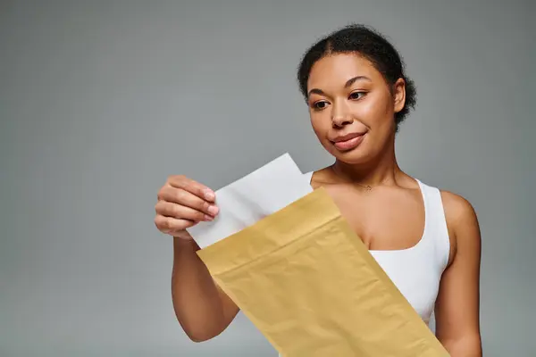 Fröhlich afrikanisch-amerikanische Diätassistentin hält Umschlag mit Ernährungsplan vor grauem Hintergrund — Stockfoto