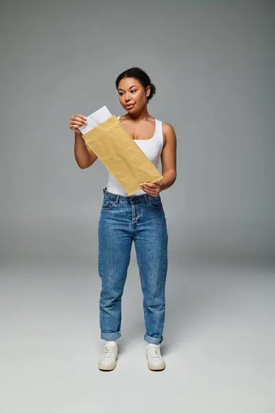 Heureuse femme afro-américaine tenant enveloppe contenant un plan alimentaire sur fond gris — Photo de stock