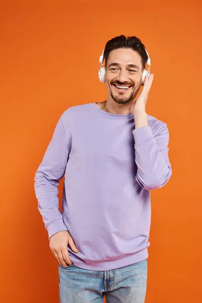 Happy bearded man in purple sweater and wireless headphones listening music on orange background — Stock Photo