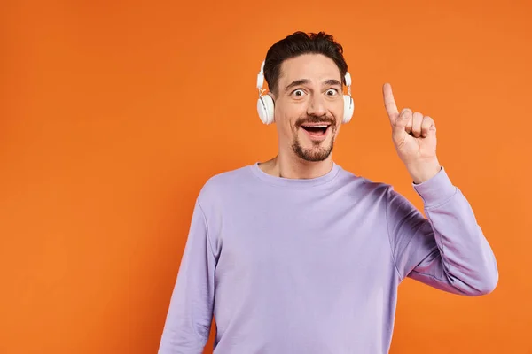 Homem barbudo espantado em fones de ouvido sem fio ouvir música em fundo laranja, gesto ideia — Fotografia de Stock