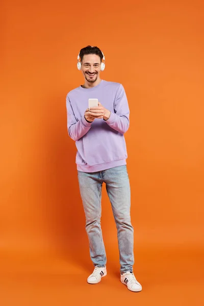 Glücklicher Mann mit drahtlosen Kopfhörern, Musik hörend und Smartphone auf orangefarbenem Hintergrund — Stockfoto