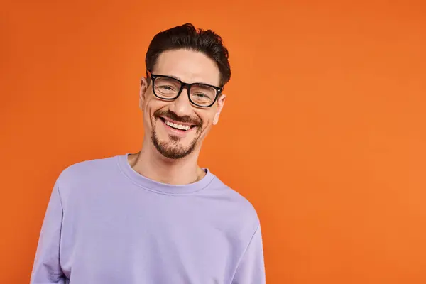 Веселий чоловік у фіолетовому светрі та модні окуляри на помаранчевому фоні, позитивні емоції — стокове фото