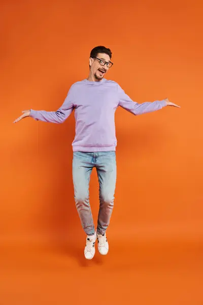 Cheerful man in eyeglasses and purple sweater levitating on orange background, flying in air — Stock Photo