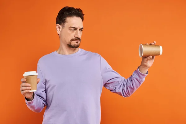 Bärtiger Mann im lila Pullover mit leerem Pappbecher auf orangefarbenem Hintergrund, Coffee to go — Stockfoto