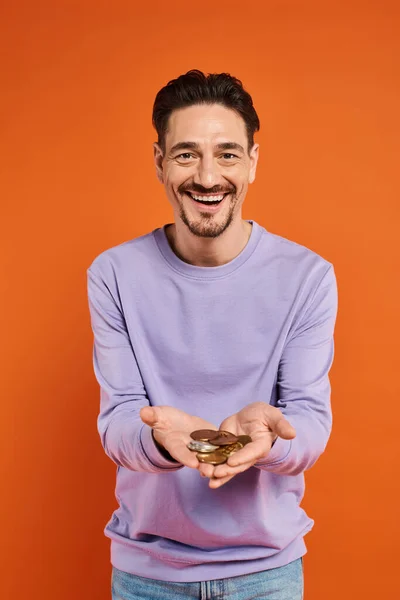 Joyful man holding bitcoins in hands and smiling at camera on orange background, cryptocurrency — Stock Photo