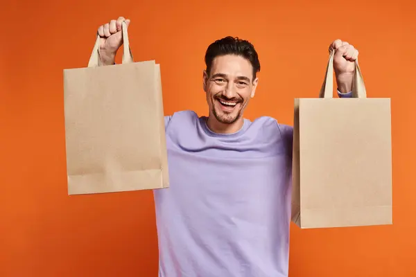 Happy bearded man in casual attire holding shopping bags on orange background, consumerism — Stock Photo