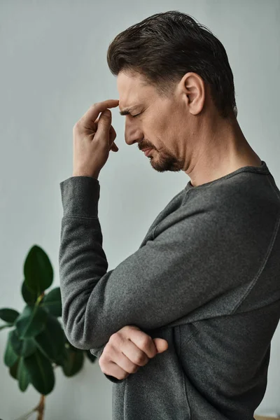 Homem estressado e barbudo com olhos fechados franzindo a testa enquanto sofre de dor de cabeça em casa, enxaqueca — Fotografia de Stock