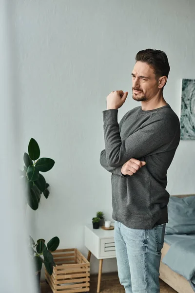 Uomo pensieroso e barbuto in maglione grigio che distoglie lo sguardo mentre è a casa, profondamente pensieroso — Foto stock