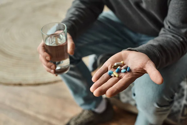 Ausgeschnittene Ansicht eines Mannes, der ein Glas Wasser und Medikamente in Händen hält, während er auf dem Bett sitzt — Stockfoto