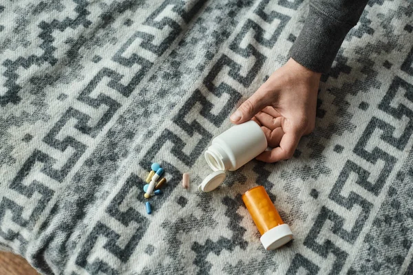 Foto recortada de la mano masculina llegar botella con medicamentos en manta gris con adorno, pastillas - foto de stock
