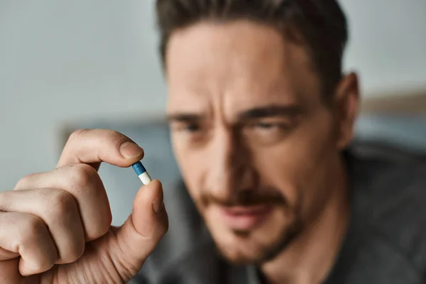 Primer plano disparo de hombre barbudo en traje casual sosteniendo cápsula azul y blanco en la mano, medicamentos - foto de stock