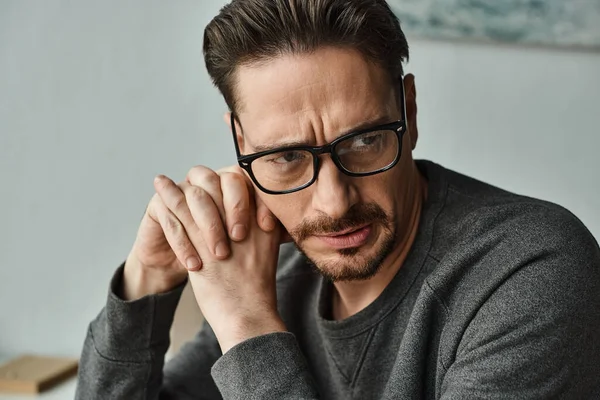 Stressed bearded man in casual wear and glasses looking away after work at home, exhausted — Stock Photo