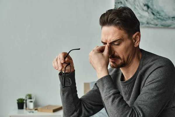 Homem barbudo estressado em uso casual segurando óculos e tocando os olhos após o trabalho em casa, burnout — Fotografia de Stock