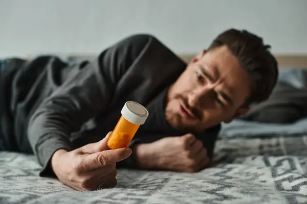 Homme barbu souffrant de douleurs abdominales et couché sur le lit près de la bouteille avec des médicaments, inconfort — Photo de stock