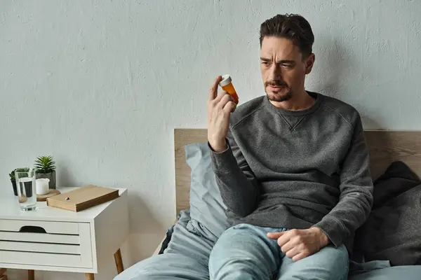 Pensive man looking at bottle with medication while sitting on bed in bedroom, treatment plan — Stock Photo