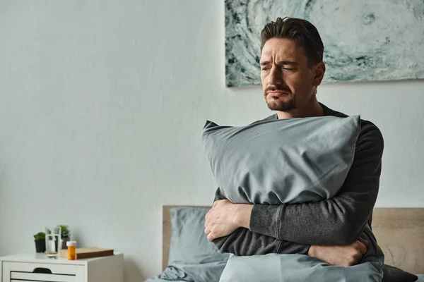 Bearded man feeling discomfort and holding pillow while sitting on bed at home, sad patient — Stock Photo
