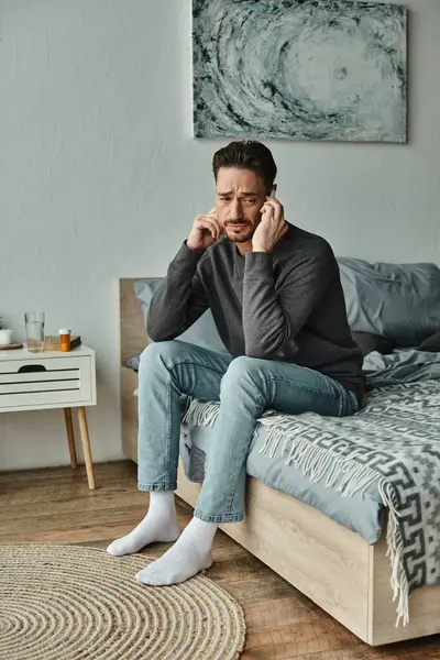Homem barbudo preocupado com dor de cabeça falando no smartphone no quarto moderno, consulta on-line — Fotografia de Stock