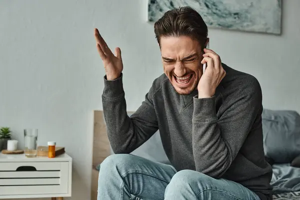 Angry bearded man in grey sweater talking on smartphone and gesturing in modern bedroom, argue — Stock Photo