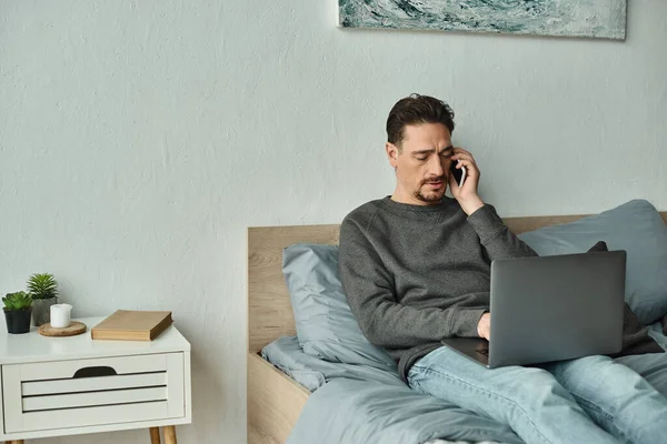 Bearded man using laptop and talking on smartphone while working remotely from home, freelance — Stock Photo