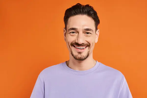 Cheerful and bearded man in purple sweater looking at camera on orange background, portrait — Stock Photo
