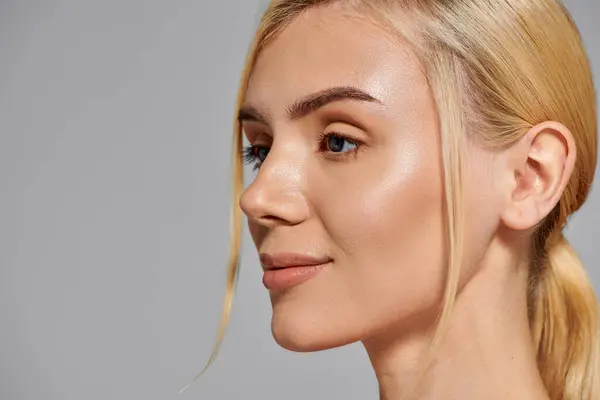 Vista de cerca de una chica guapa rubia de 20 años con mirada confiada en fondo gris - foto de stock