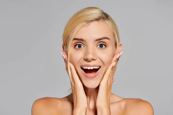 Excited girl with blonde hair and gray eyes showing surprise face expression on gray background — Stock Photo