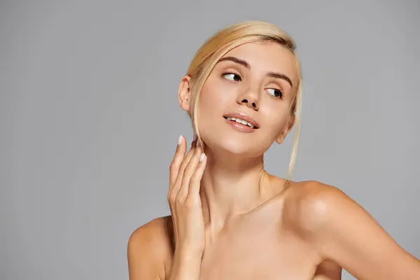 Charming woman with perfect skin looking to side and touching neck with hand in gray background — Stock Photo