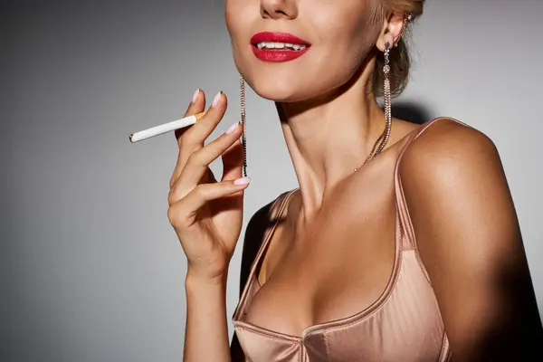 Cropped view of glamourous girl with red lips and cigarette smiling against grey background — Stock Photo